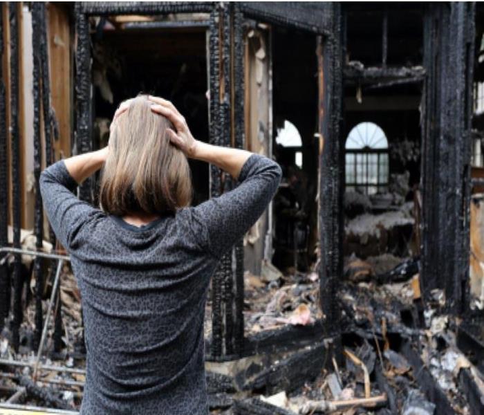 Woman with hands on her head looking at a burnt house